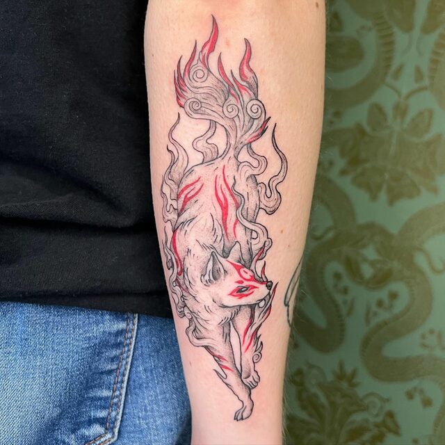 Tattoo of Amaterasu, the white wolf from the game Ōkami, with red markings and flames, on a forearm