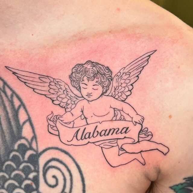 Fine-line tattoo of a winged cherub holding a banner reading Alabama, on a chest