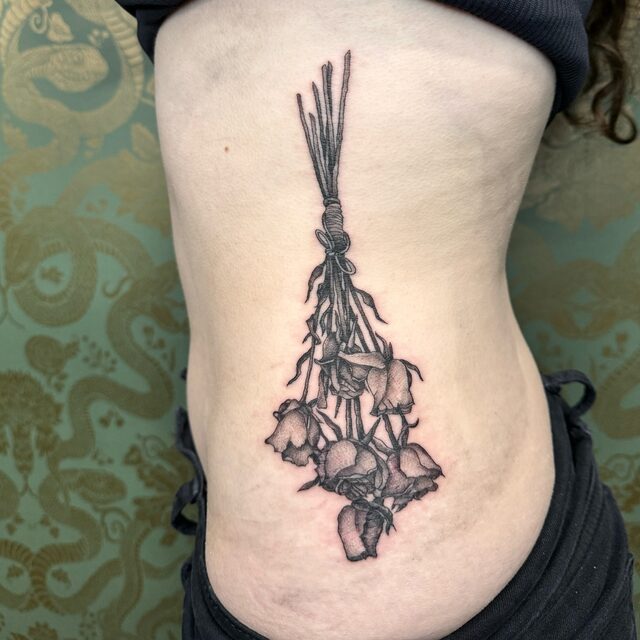 Stippled tattoo of a bunch of roses hanging upside down, tied with string, on the ribs