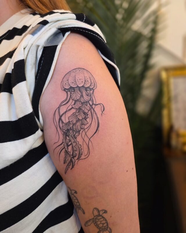 Delicate etched jellyfish with trailing tentacles, tattooed on an upper arm