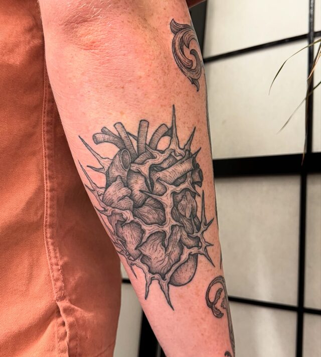 Anatomical heart wrapped in thorny vines, tattooed on a forearm