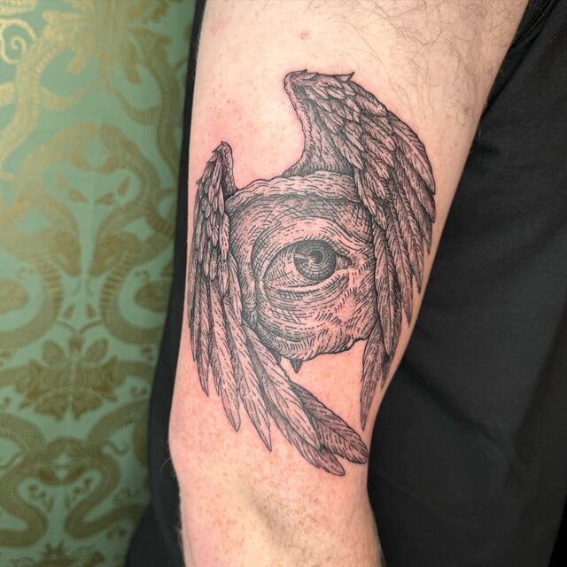 An eye framed by feathered wings, tattooed on an upper arm